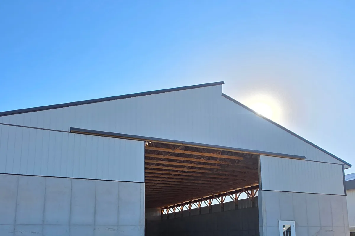 New pole building seen from outside, with the open bay door showing the timber roof framing