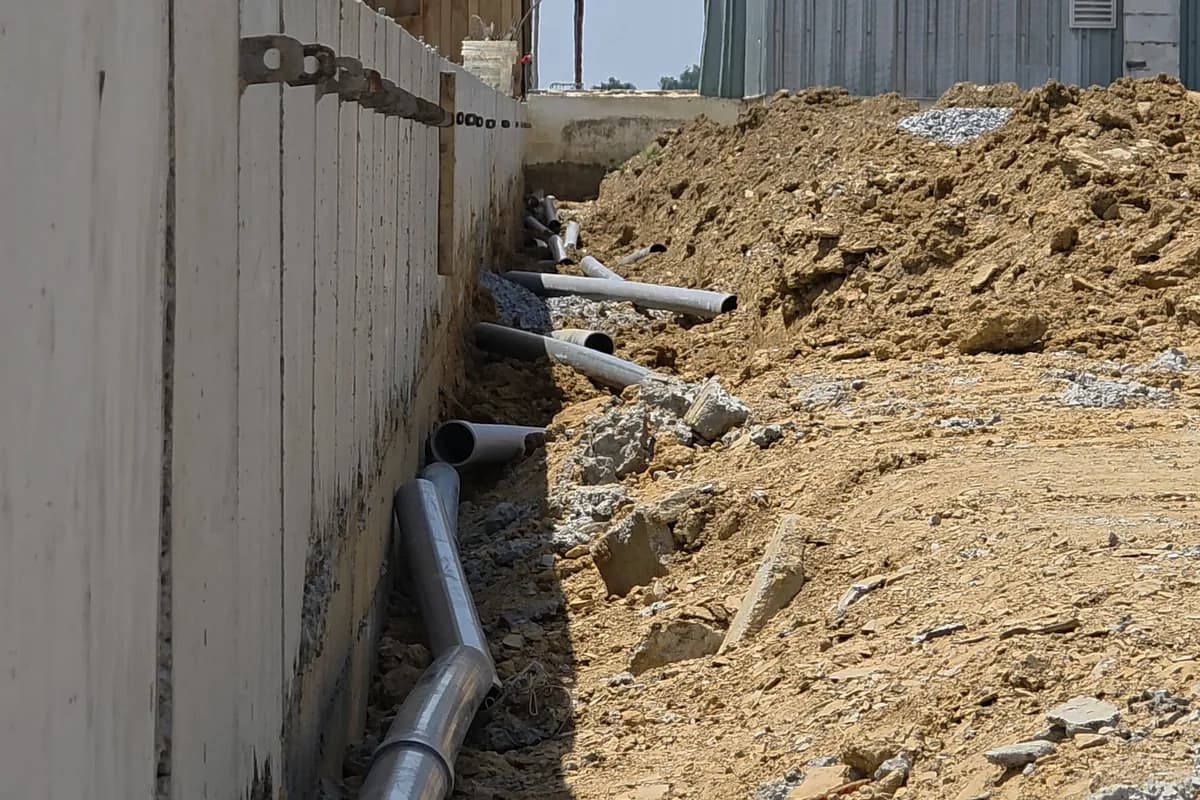 Open trench running along a farm building with conduit laid in